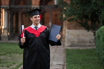 Graduate guy in graduation gown with diploma in his hands in campus