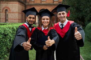 Group of graduate students in graduation gowns show like at camera