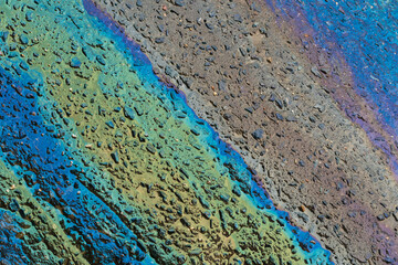 Multicolored gasoline oil stains on the asphalt road surface texture or background