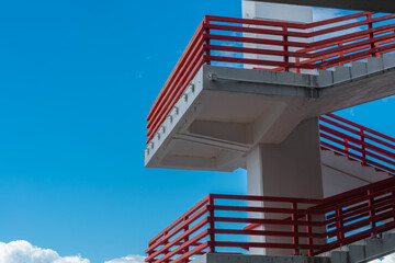 Concrete structure with staircase and red metal railings against blue sky and cloud, pattern or background