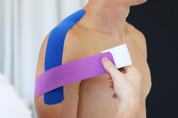 Kinesiology taping. Physical therapist applying kinesiology tape to patient shoulder. Male therapist treating injured shoulder of male athlete. Post traumatic rehabilitation, sport physical therapy. - obrazy, fototapety, plakaty