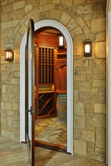 Open wooden door leading to stone cellar with barrel and wooden shelves