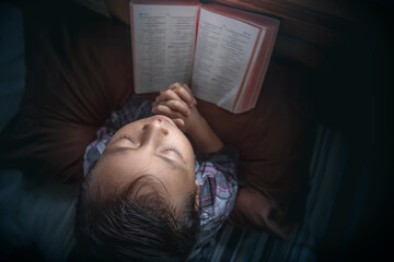 Top down view little girl praying on the bed with bible in home. Christian prayer concept.