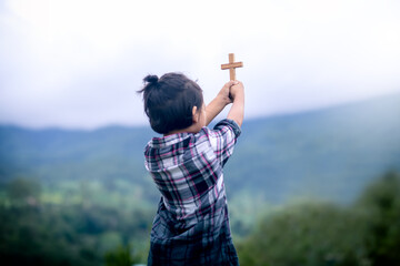 A little girl praying and holding wooden cross, focus at the cross, Christian little girl concept.
