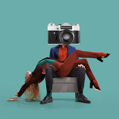 Young flexible woman lies in arms of a man with disco retro-style camera instead of head sitting in armchair over blue-green background