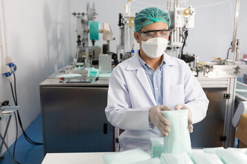 male factory worker holding packaging a lot of medical face masks and checking of quality from machine