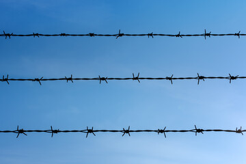 Barbed wire with blue sky in the background. It is a type of steel fencing wire constructed with sharp edges or points arranged at intervals along the strands. 