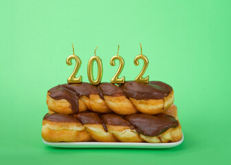 Chocolate frosted glazed twist donuts stacked on a rectangular plate green background with gold 2022 candles. Happy New Year theme.