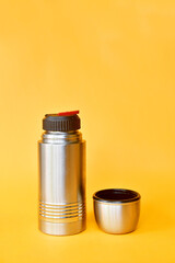 Small water thermos in silver color isolated on yellow background
