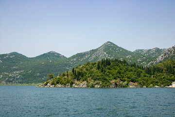 Fototapeta premium Landscape with lake and green mountains against the background of a clear sky. Panoramic beautiful view on largest lake. Wonderful summer day.