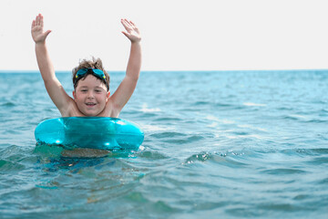 Funny little boy swims in the sea in a blu inflatable ring.