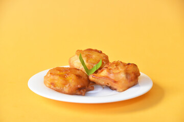 Crispy fried banana served on small white plate on color background