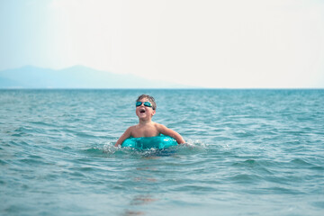Cute smiling boy having fun in the sea  and swimming with  inflatable ring.