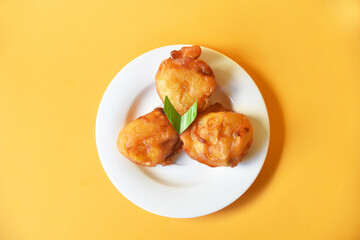 Crispy fried banana served on small white plate on color background