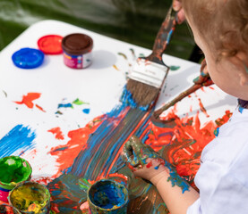 Obraz premium A small child learns to paint with his parents on a white sheet of paint.