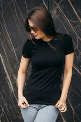 Stylish brunette girl wearing black t-shirt and glasses posing against street , urban clothing style. Street photography