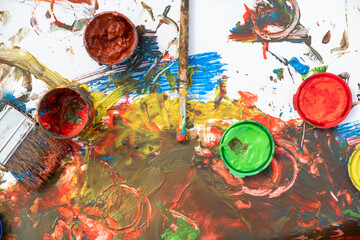 Paint cans and paint brushes in paint on a white sheet of paper. Top view.