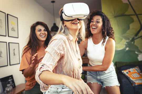 Female friends using virtual reality device at home. They're laughing and having fun.	