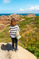 Naklejka premium A young woman on the coast next to Lighthouse Mean Ruz, port of Ploumanach, in the town of Perros-Guirec, Cotes-d'Armor, in French Brittany, France.