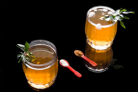 Front view of Kahwa,an Indian Kashmiri green tea made from herbal leaves,saffron and cinnamon. Glasses filled with ice cubes .Sweet,refreshing and healthy golden drink on a black background.
