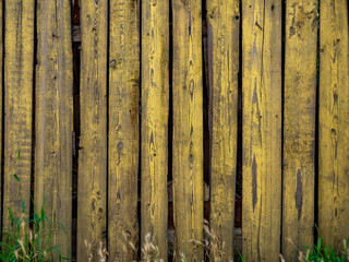 Old wooden fence made of boards painted with yellow paint.