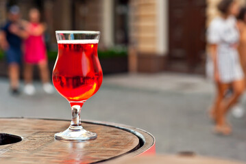 Glass of red wine close up. Alcoholic liqueur on a wooden barrel on a background of the city. Blurred people in the background.
