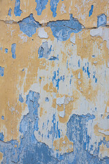 Peeling paint on the wall. Concrete wall with old yellow and blue cracked peeling paint