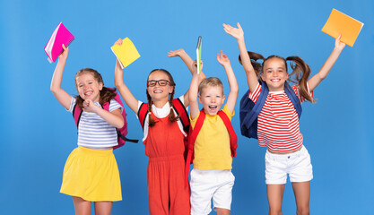 Funny kids with backpacks behind happily jumping raising their hands up with exercise books