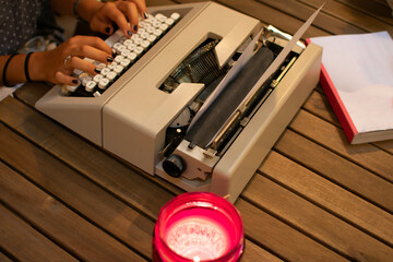 Caucasian teen hands writing on a retro typewriter. With a candle and a book.