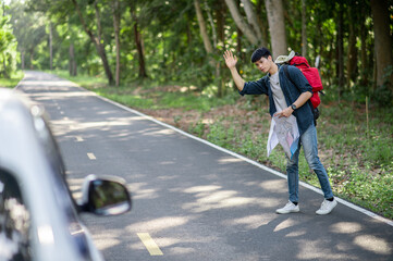 Handsome young backpacker man with map hitchhiking on road