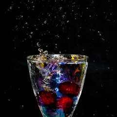 splash of liquid in rainbow sparkling glass with cherries on black background, low key
