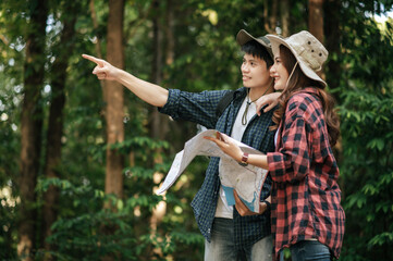 Young trekking couple use map while walking on forest trail