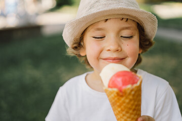 Boy in a hat is holding an ice cream and looks happy and surprised. Summer food and summer time