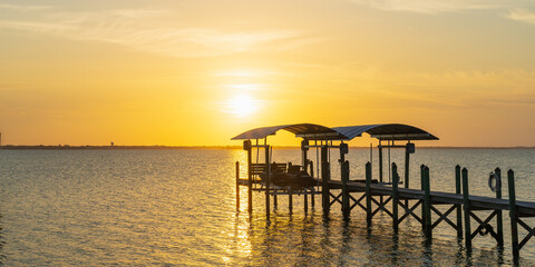 Obraz premium View of a sunset over a wooden pier in Indian River, Florida from the A1A. Wooden pillars of the old pier near the coast as a typical view of Florida 
