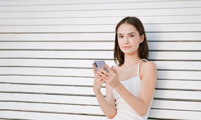 Beautiful young girl sitting on a bench and chatting on a mobile phone