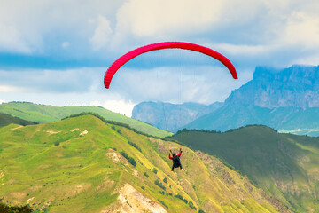 A red paraglider flies in the mountains. Paragliding flights
