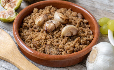 Close-up of a typical Spanish dish called Migas, accompanied by grapes and figs, on a rustic wooden background.