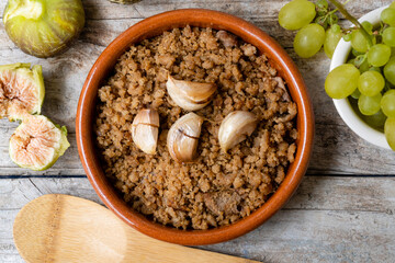 Close-up of a typical Spanish dish called Migas, accompanied by grapes and figs, on a rustic wooden background.