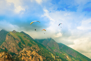 Paragliders fly over the mountains in a beautiful cloudy sky. Paragliding flight in the mountains