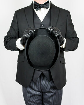 Portrait of British Gentleman in Dark Suit and Leather Gloves Holding Bowler Hat on White Background. Concept of Butler and Professional Hospitality. 