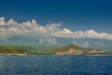 Obraz premium Seacoast with high mountains on a sunny day, with clouds hanging over the mountains