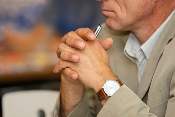 Man's hands clasped in the lock hold a pen. The man is silent and thoughtful. Businesswoman in shirt and suit