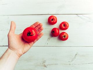 Male hand holding a fresh healthy tomato, white wooden background. Additional place for text.
