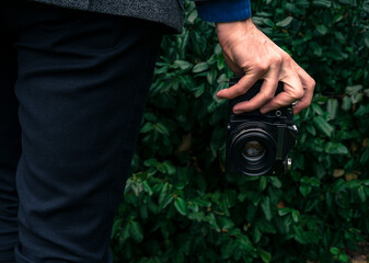 Male hand holding a vintage film camera in the air. Green nature in the background.