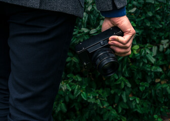 Male hand holding a vintage film camera in the air. Green nature in the background.
