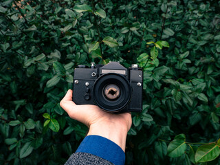 Male hand holding a vintage film camera in the air. Green nature in the background.