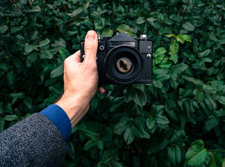 Male hand holding a vintage film camera in the air. Green nature in the background.