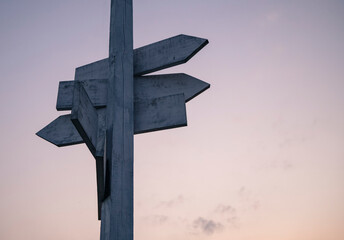 White wooden signpost with a sky during sunset in the background.
