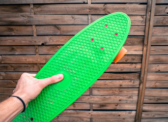 Male hand holding a green penny board in a skatepark.