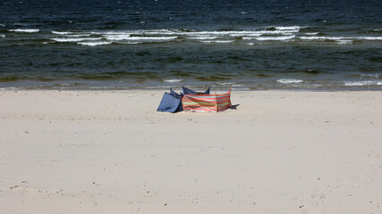 Widok na piaszczystą plażę nad morzem z parawanami.